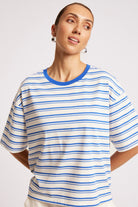 A woman wearing a short-sleeve crewneck t-shirt with thin blue horizontal stripes on an off-white background, featuring a solid blue collar.