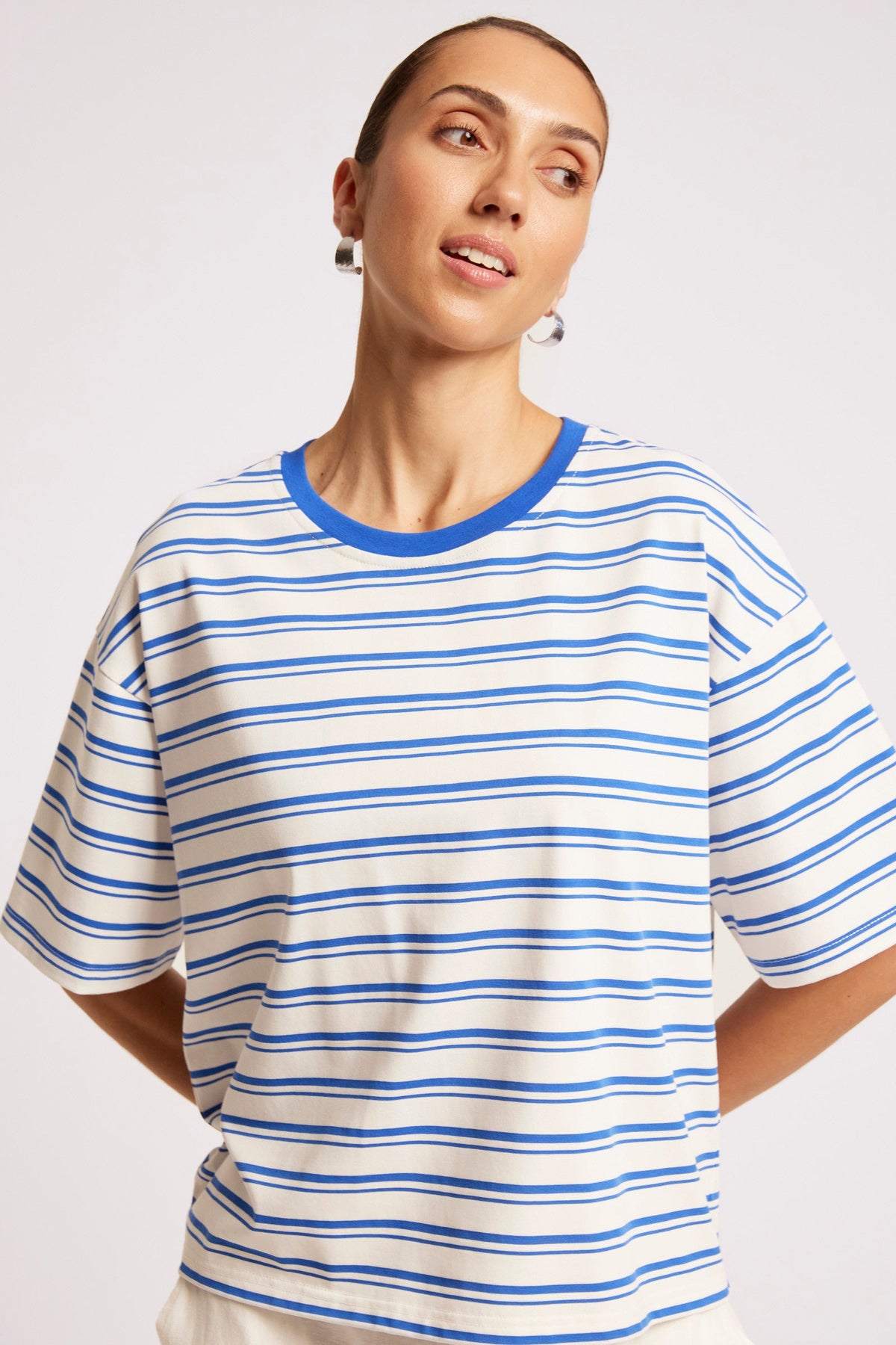 A woman wearing a short-sleeve crewneck t-shirt with thin blue horizontal stripes on an off-white background, featuring a solid blue collar.