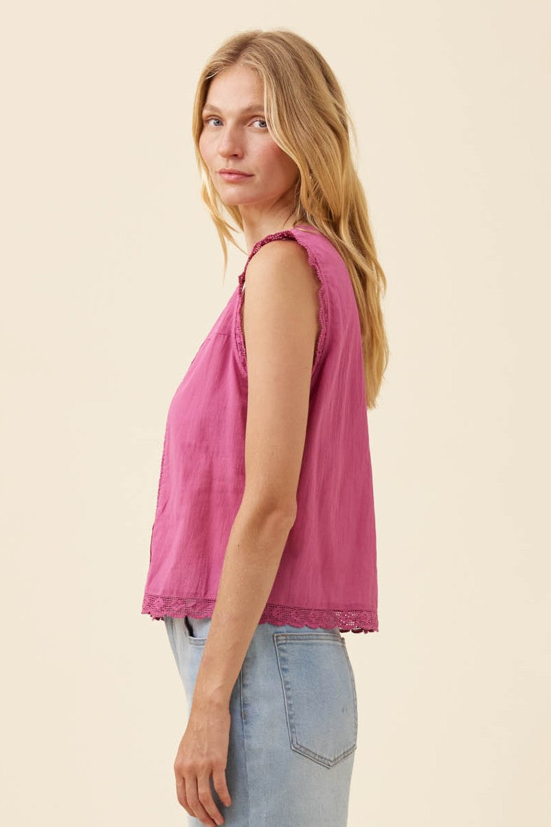A woman shown in side profile wearing a sleeveless dusty pink top with delicate lace trim at the neckline and hem, paired with light blue jeans, against a solid cream background.