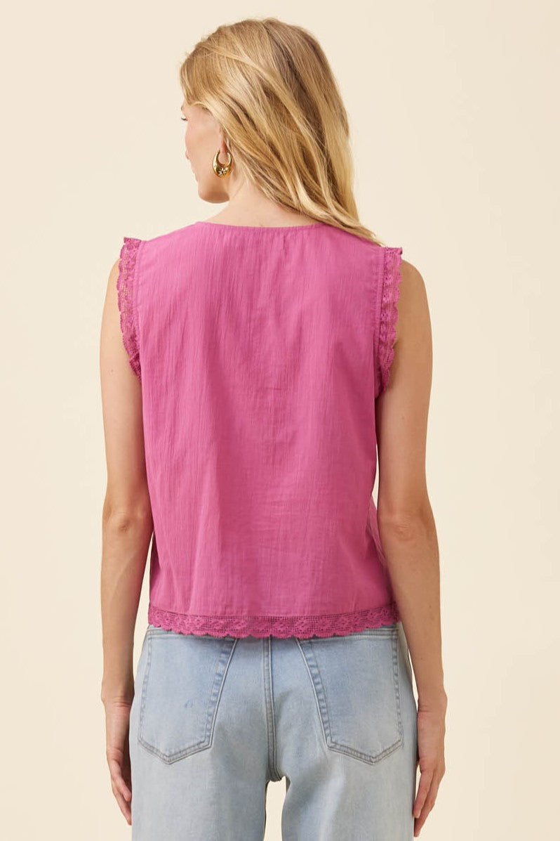 A woman shown from the back wearing a sleeveless pink top with scalloped edges and light blue jeans, against a plain beige studio background.