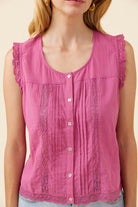 A sleeveless pink blouse with a scoop neckline, button-front center, vertical gathered pleats, and lace trim at the shoulders and hem, shown on a model against a light beige background.