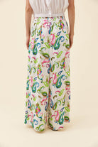 A model is shown from the waist down wearing high-waisted, wide-leg trousers with a vibrant multicolor paisley pattern on a cream background.