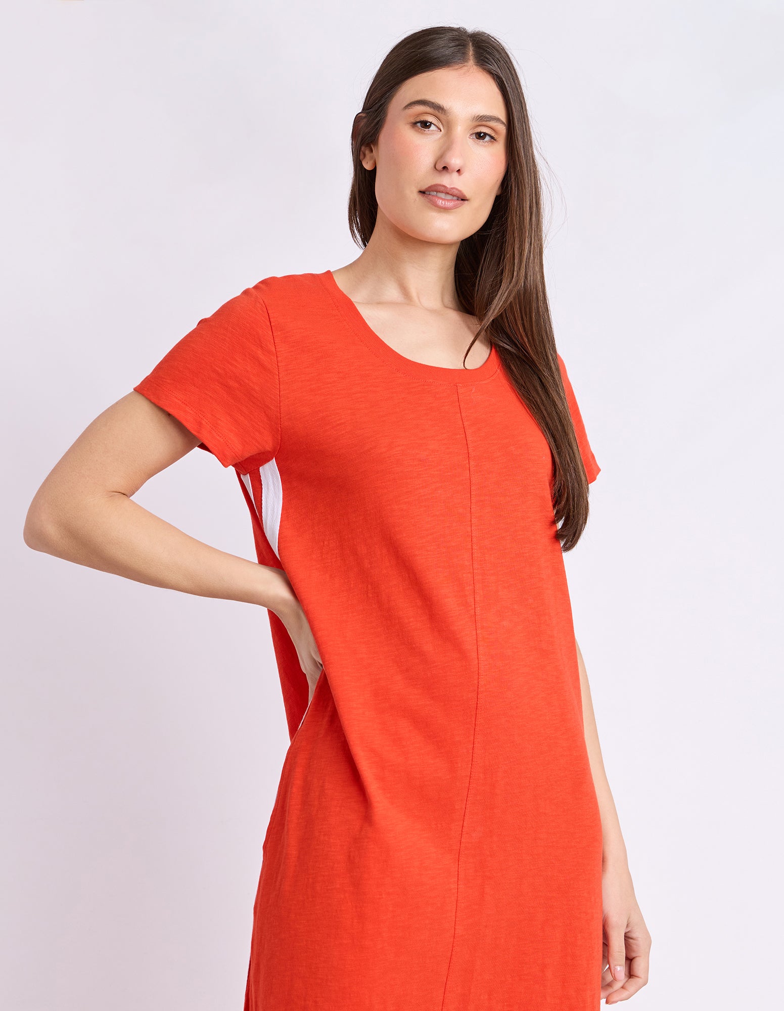 A woman modeling a bright orange short-sleeve tunic dress with side cutouts, photographed against a plain light gray studio background.