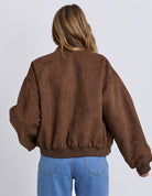 Person wearing a brown jacket and blue jeans on a white background