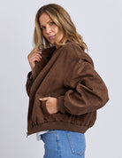 Woman wearing a brown jacket and blue jeans on a white background