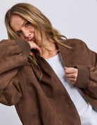 Woman wearing a brown suede jacket over a white shirt on a light gray background