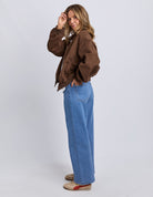 Person wearing a brown jacket and blue jeans on a white background