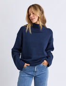 Woman wearing a navy sweater and blue jeans against a light gray background
