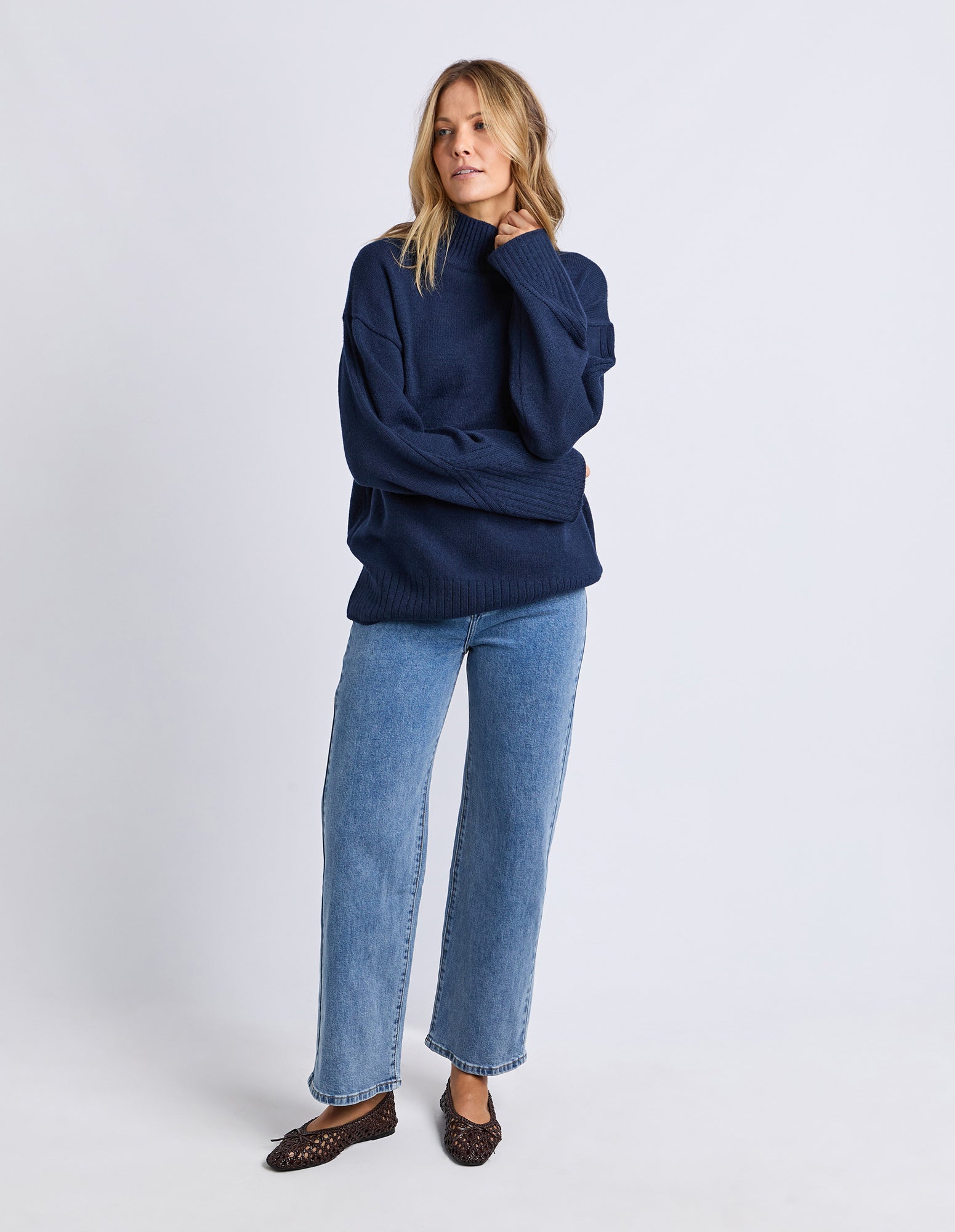 Woman wearing a navy sweater and blue jeans on a white background