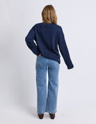Person wearing a navy sweater and blue jeans on a white background