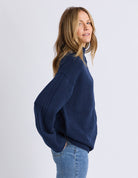 Woman wearing a navy sweater and jeans on a white background
