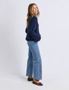 Woman wearing a navy sweater and light blue jeans on a white background
