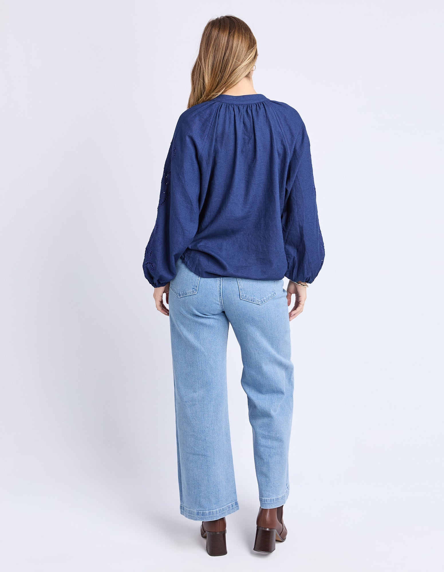 Person wearing a blue blouse and light blue jeans on a white background
