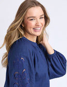 Woman wearing a blue blouse with intricate designs on a white background