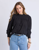 Woman wearing a black blouse and blue jeans on a light gray background