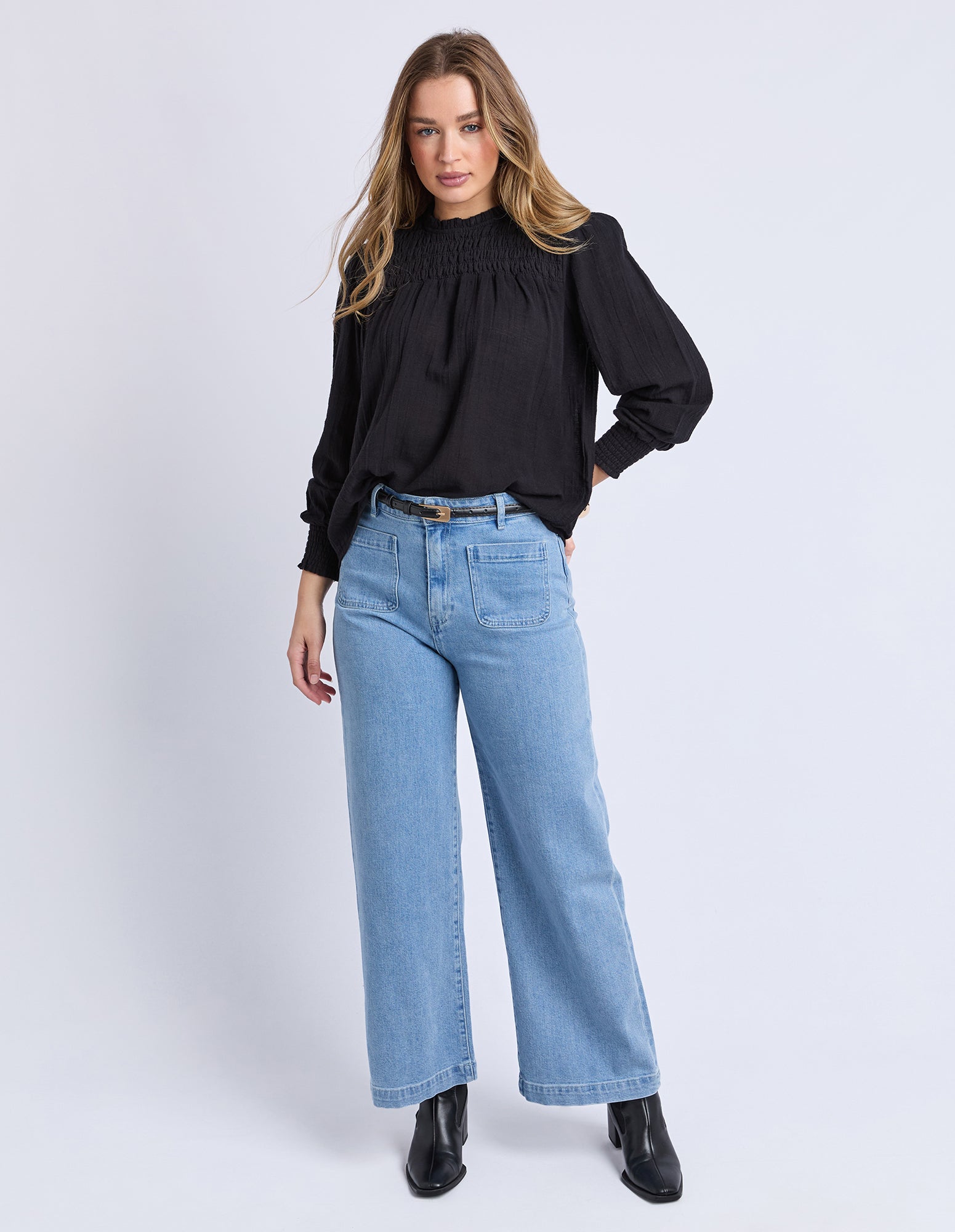 Woman wearing a black top and light blue jeans on a white background
