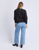 Person wearing a black top and light blue jeans on a white background