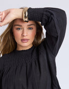Woman wearing a black top with puffed sleeves against a light gray background