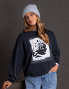 Woman wearing a black sweatshirt with a floral design and a gray beanie against a dark background