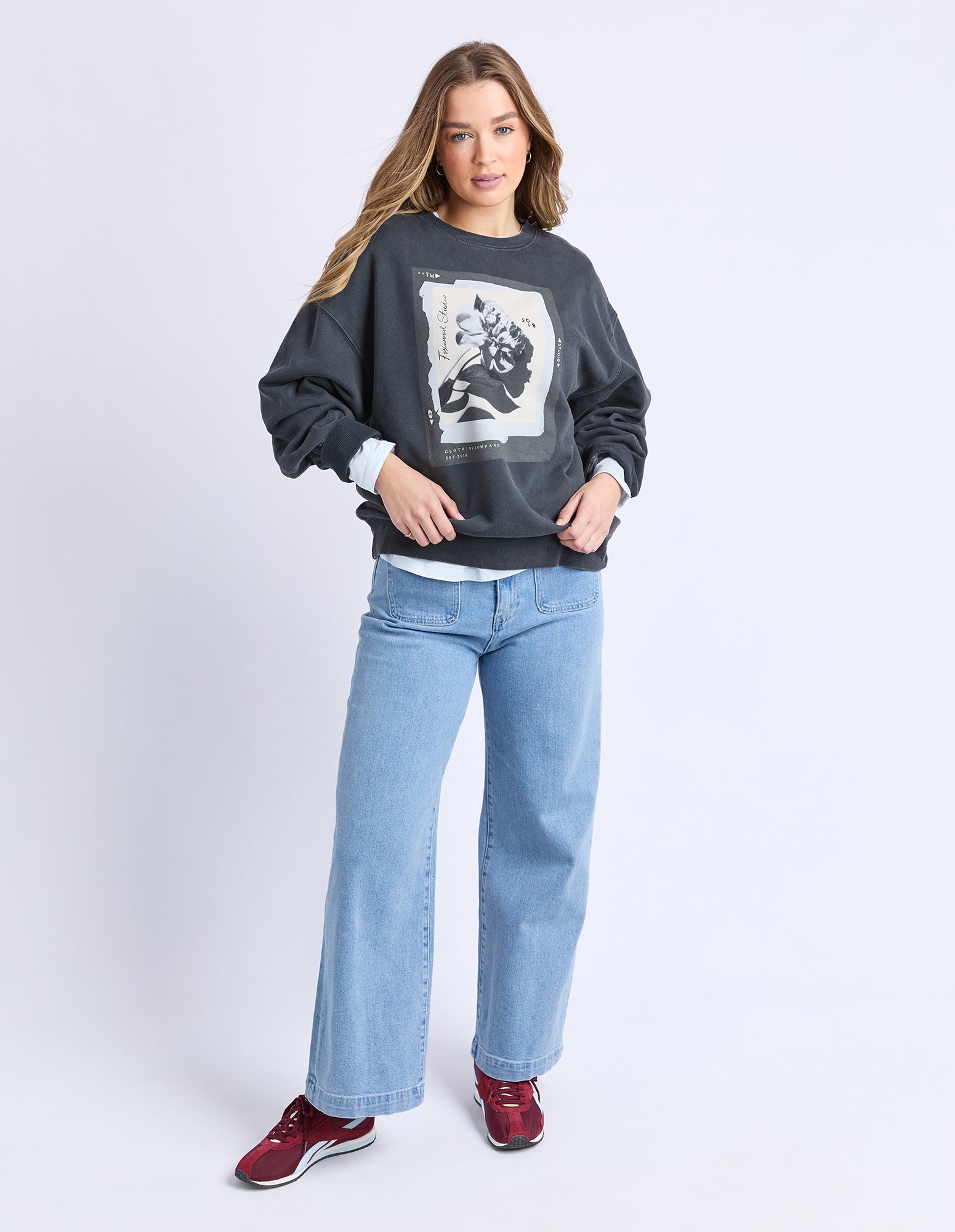 Woman wearing a dark gray sweatshirt with a graphic design and light blue jeans on a white background
