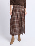 Person wearing a brown plaid skirt with a brown sweater and boots on a white background