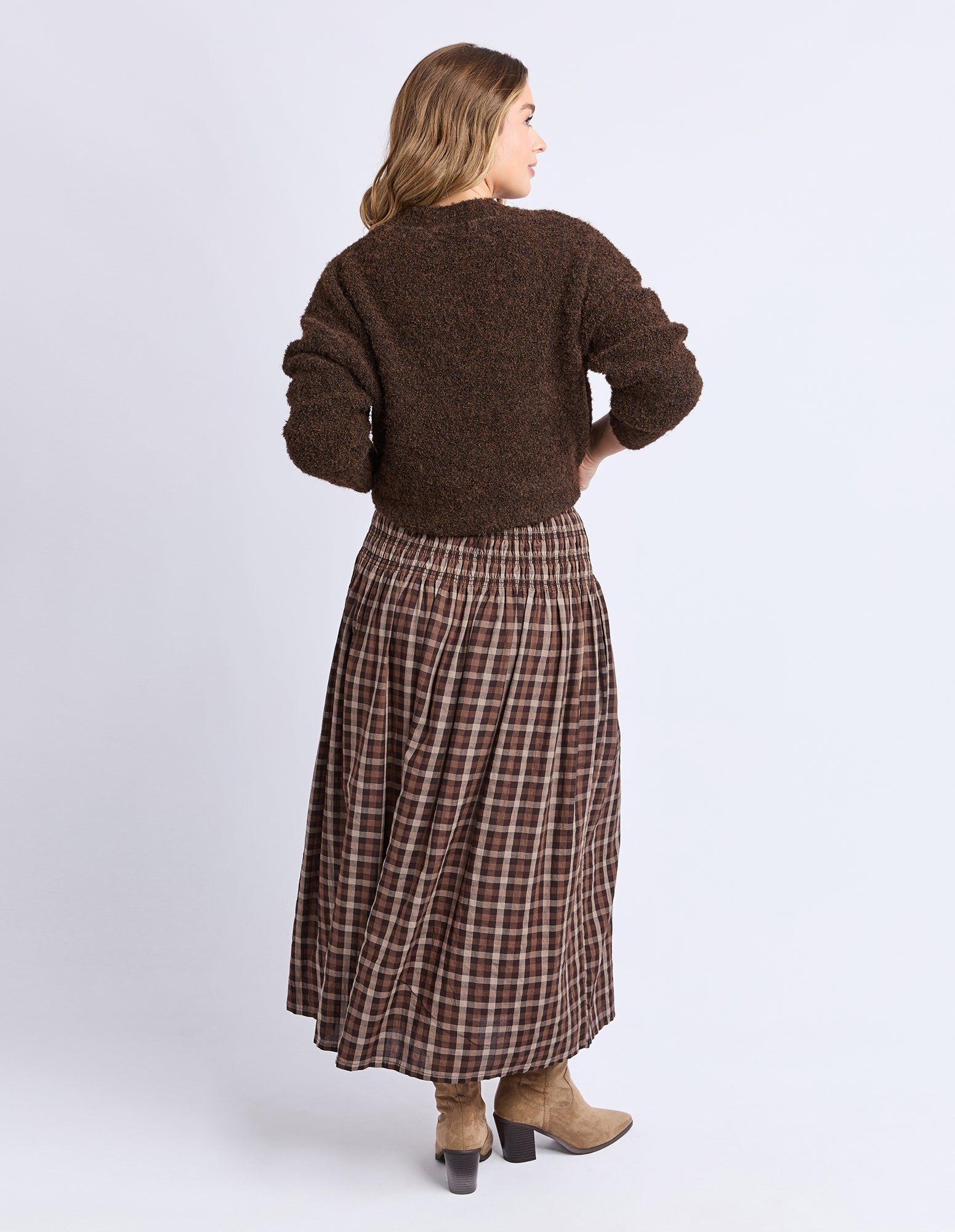 Woman wearing a brown sweater and plaid skirt on a white background