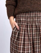 Brown plaid pants worn with a brown sweater on a light gray background