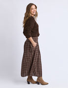 Woman wearing a brown sweater and plaid pants on a white background