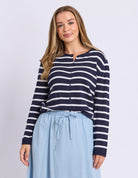 Woman wearing a navy and white striped shirt with a light blue skirt on a plain background
