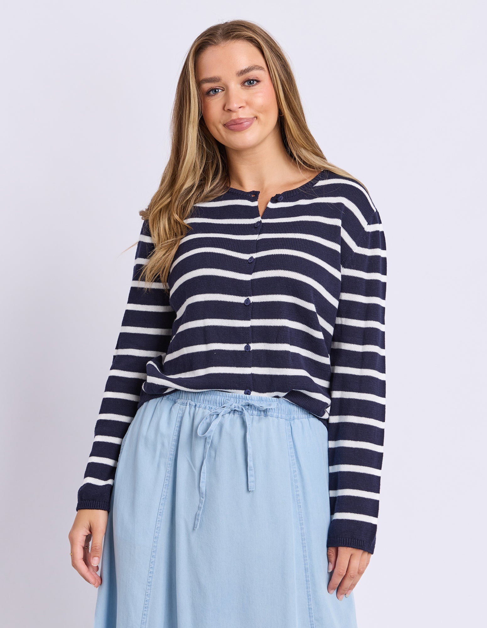 Woman wearing a navy and white striped shirt with a light blue skirt on a plain background