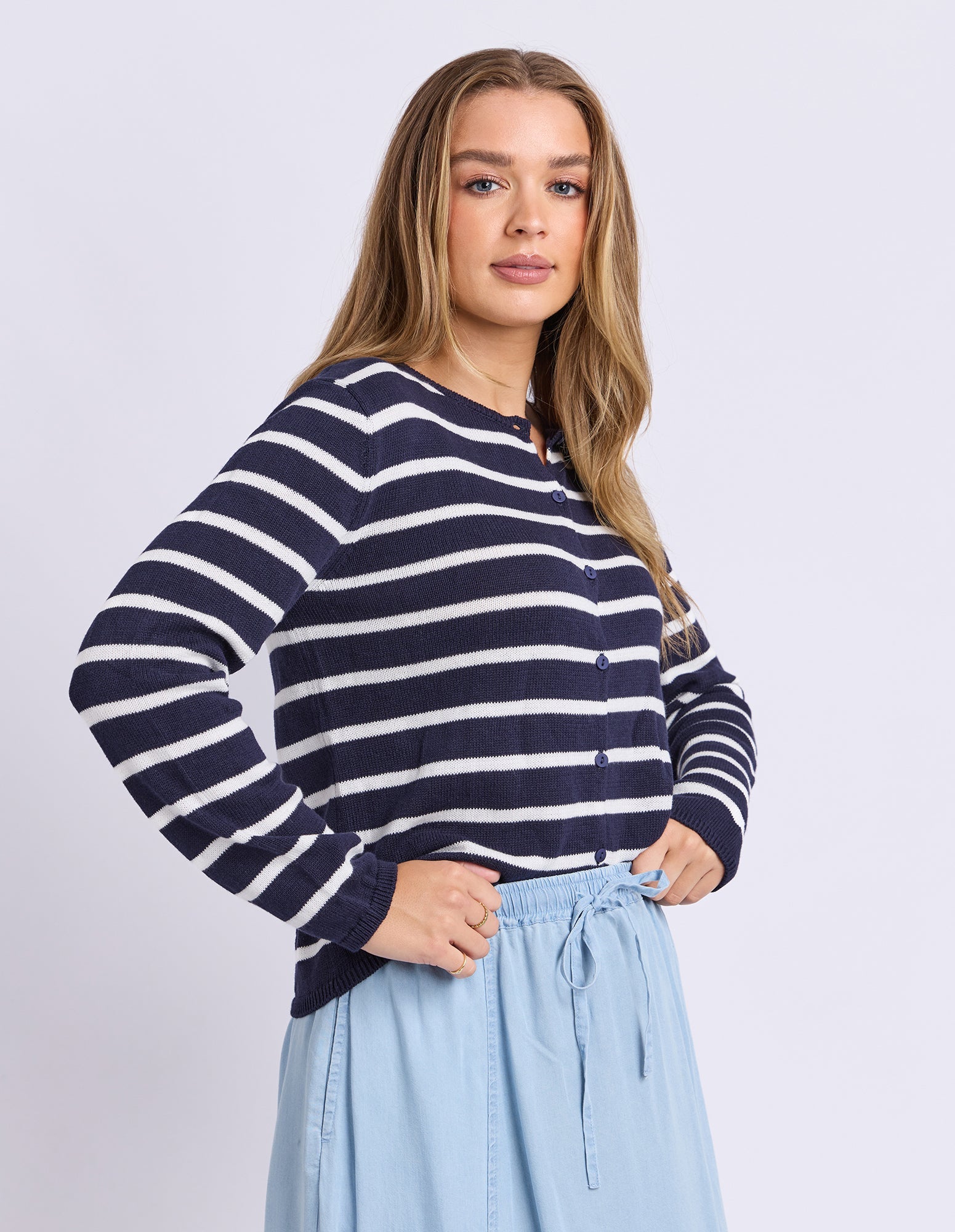 A woman modeling a navy and white horizontally striped long-sleeve knit top with a buttoned round neckline, paired with light blue drawstring skirt pants, against a light gray studio background.