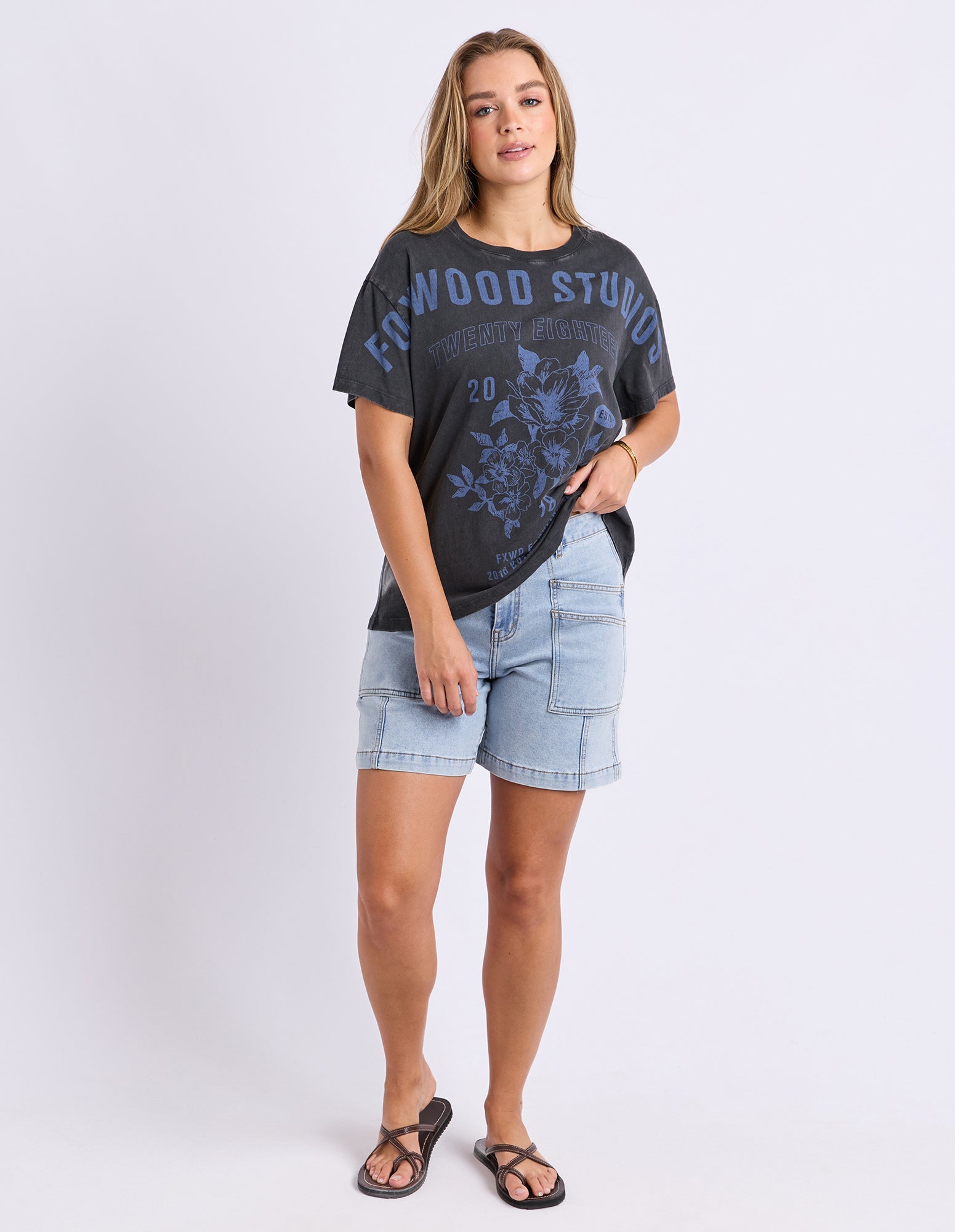 Woman wearing a black graphic t-shirt and denim shorts on a white background