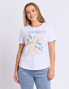 Woman wearing a white t-shirt with floral design and 'FOXWOOD' text on a light gray background