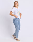 Woman wearing a white t-shirt with a colorful design and light blue jeans on a white background
