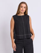 Woman wearing a black sleeveless top with white stitching on a light gray background