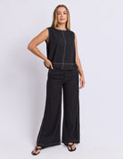 Woman wearing a black sleeveless top and wide-leg pants on a white background