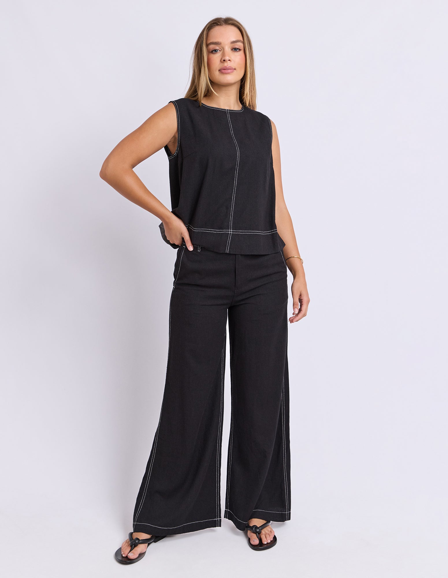 Woman wearing a black sleeveless top and wide-leg pants on a white background