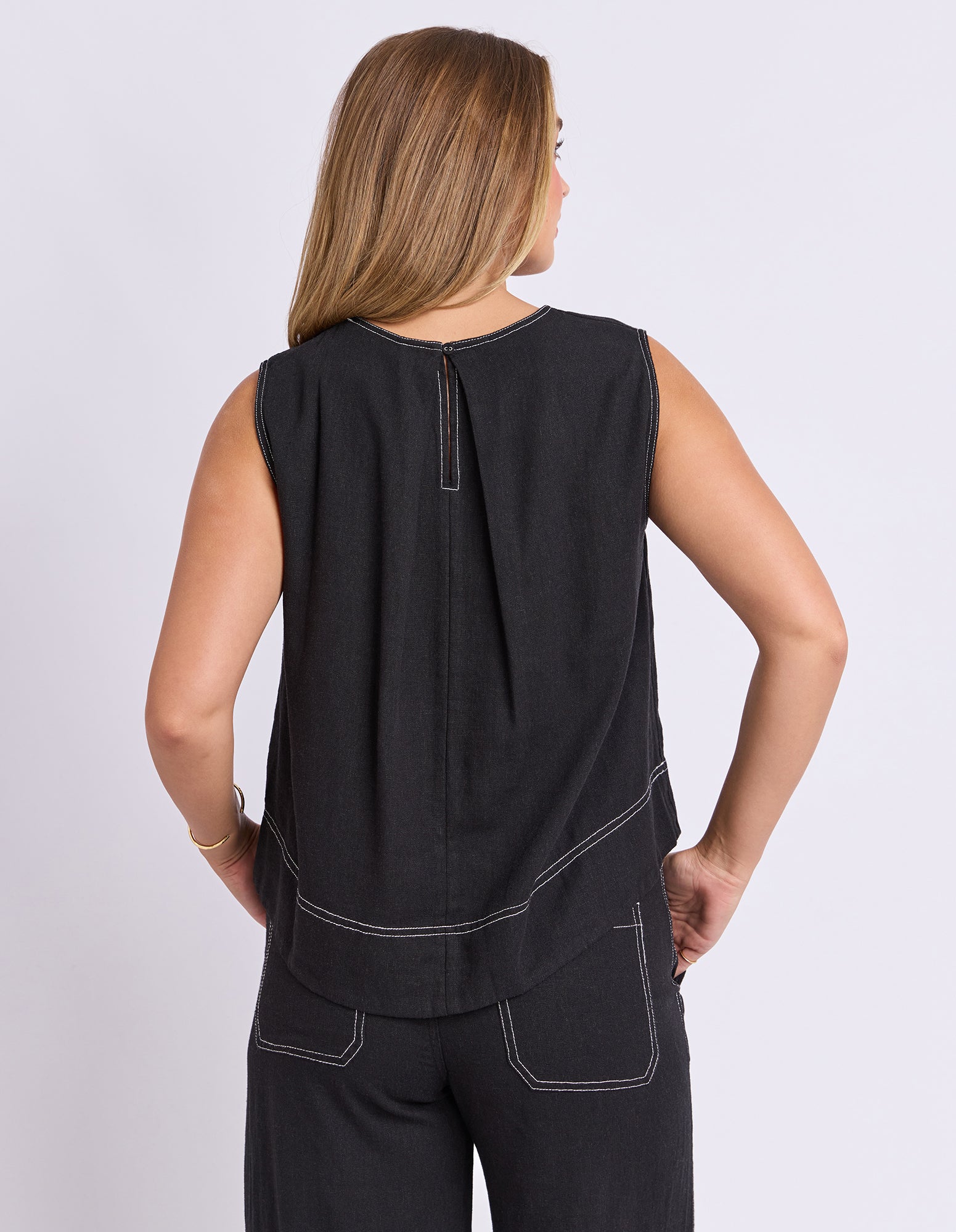 Woman wearing a black sleeveless top and pants on a light gray background