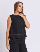 Woman wearing a black sleeveless top and pants on a light gray background