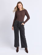 Woman wearing a brown long-sleeve top and black jeans on a white background