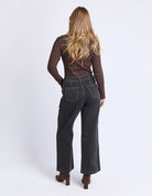 Woman wearing black jeans and a brown top on a white background
