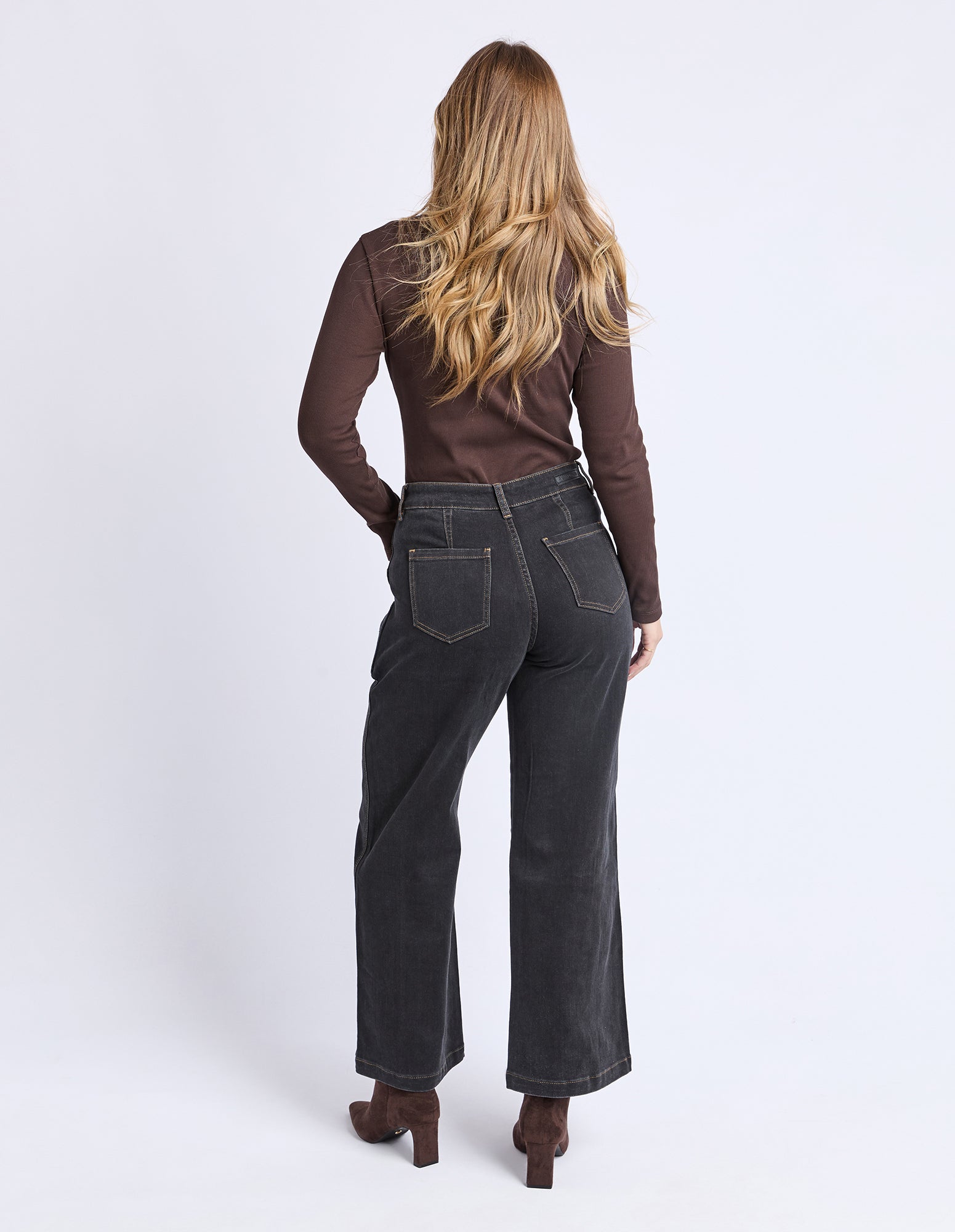 Woman wearing black jeans and a brown top on a white background