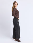 Woman wearing a brown long-sleeve top and black wide-leg jeans on a white background