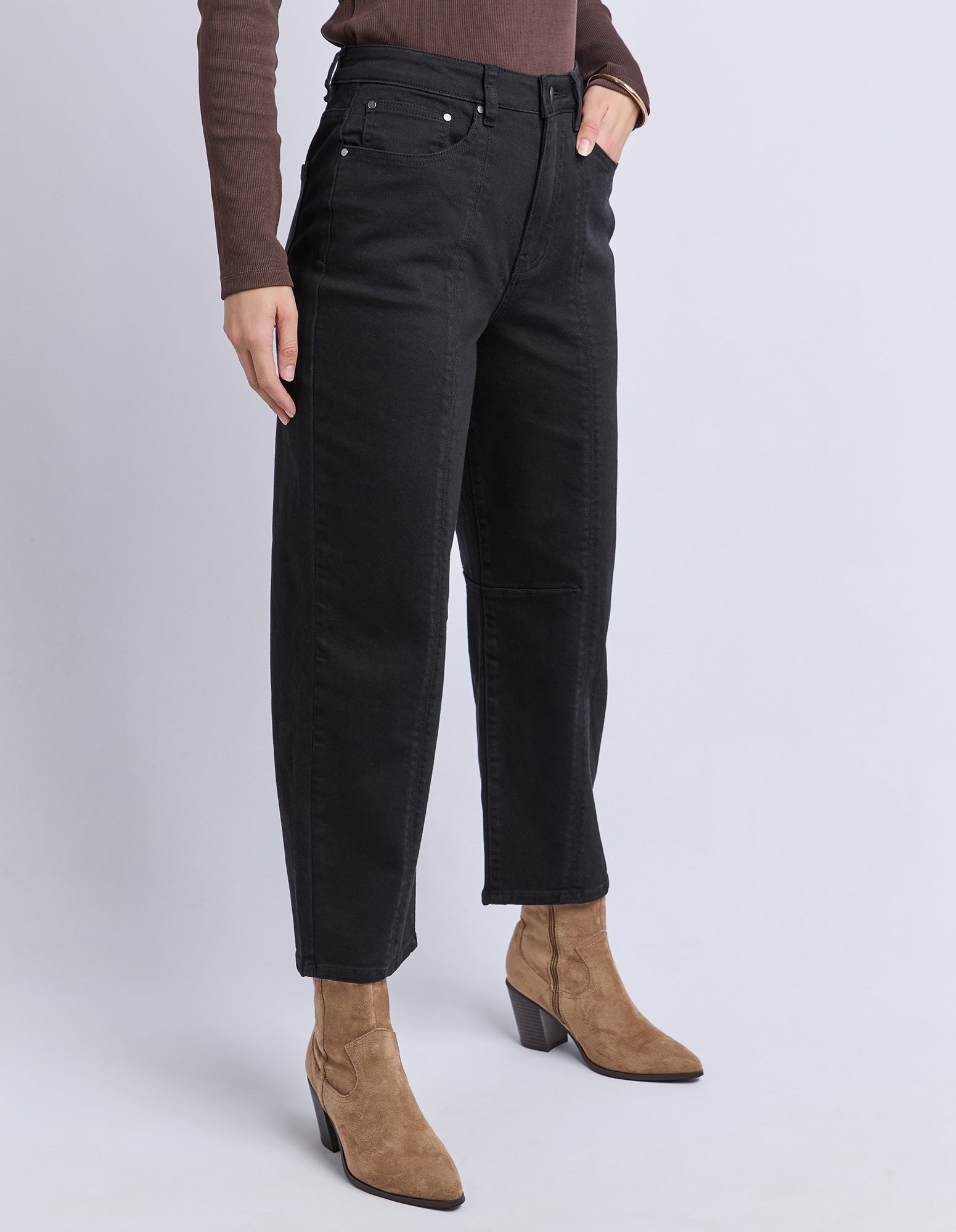 Person wearing black pants and brown boots on a white background