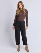 Woman wearing a brown long-sleeve top and black pants on a white background