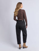 Woman wearing a brown top and black pants on a light gray background