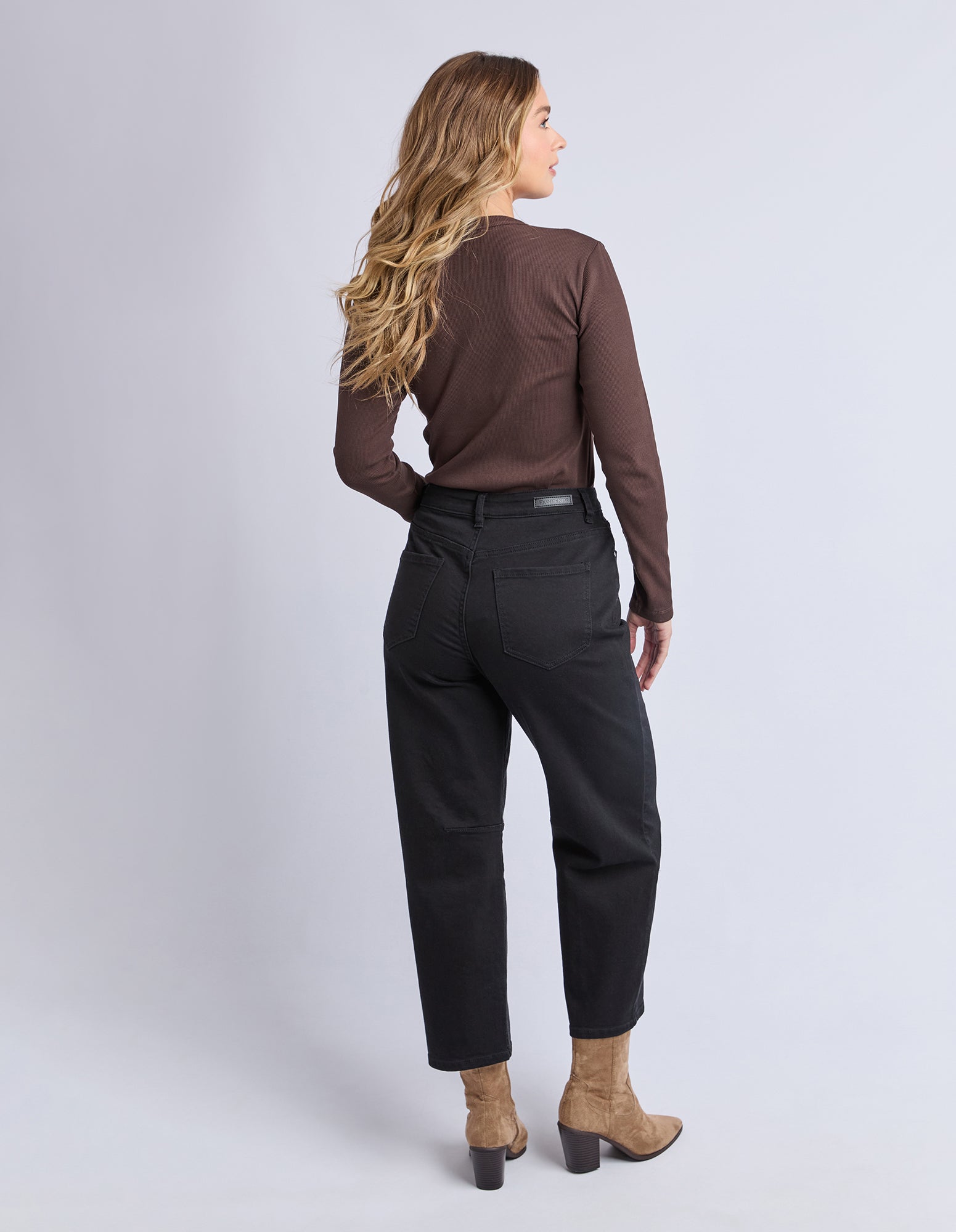 Woman wearing a brown top and black pants on a light gray background