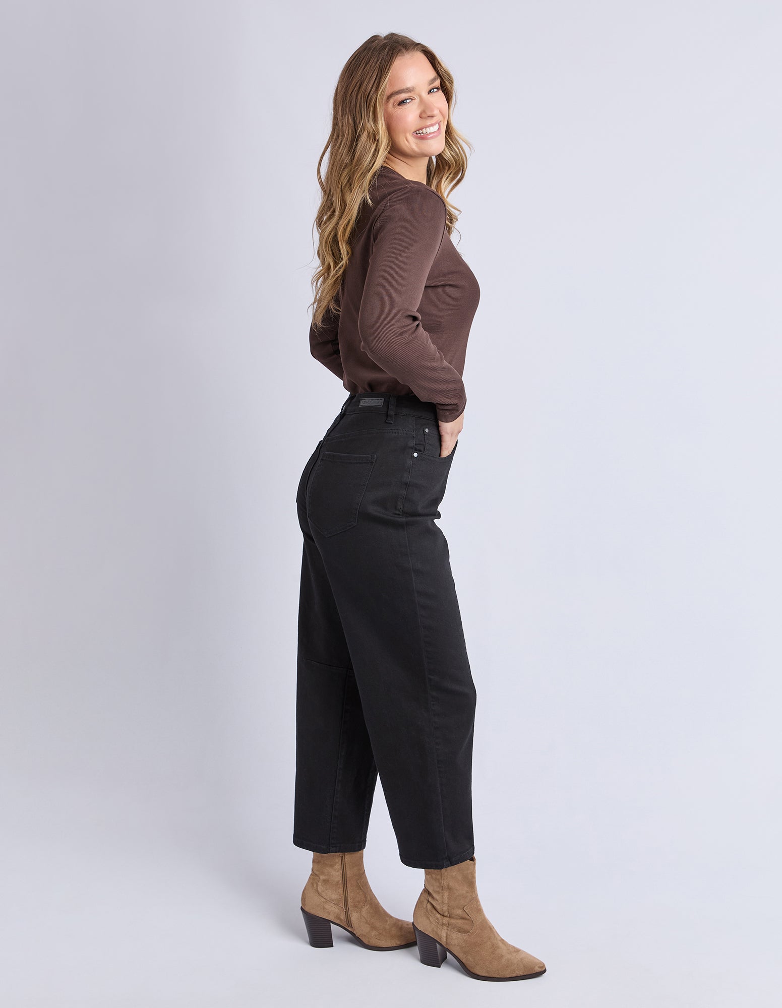 Woman wearing a brown top and black pants on a light gray background