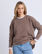 Woman wearing a brown sweatshirt and blue jeans on a white background