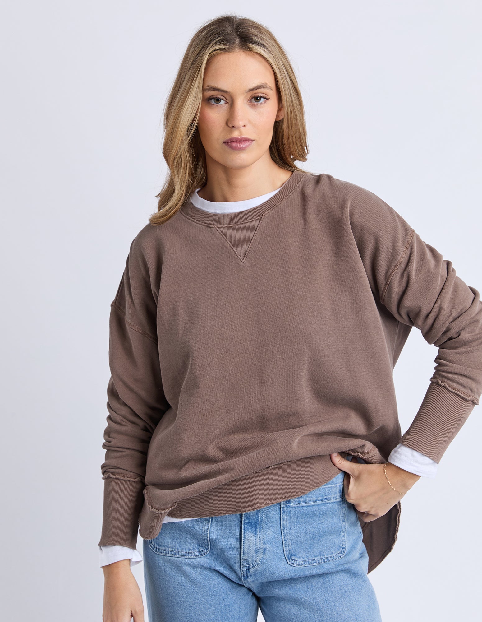 Woman wearing a brown sweatshirt and blue jeans on a white background